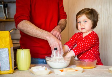 Mavi gözlü ve kırmızı elbiseli şirin bir kız karantina sırasında mutfakta undan pasta yapıyor.
