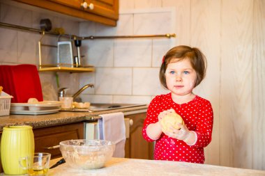 Mavi gözlü ve kırmızı elbiseli şirin bir kız karantina sırasında mutfakta undan pasta yapıyor.