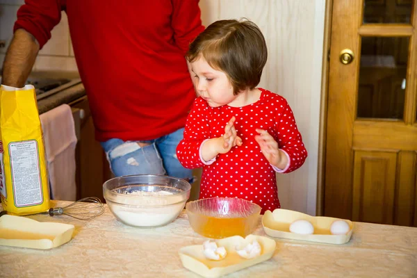 a cute little girl with blue eyes and red clothes is making cakes out of flour in the kitchen at home during the quarantine