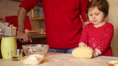 Kırmızı elbiseli küçük bir kız, evde, mutfakta, karantina sırasında undan pasta yapıyor.