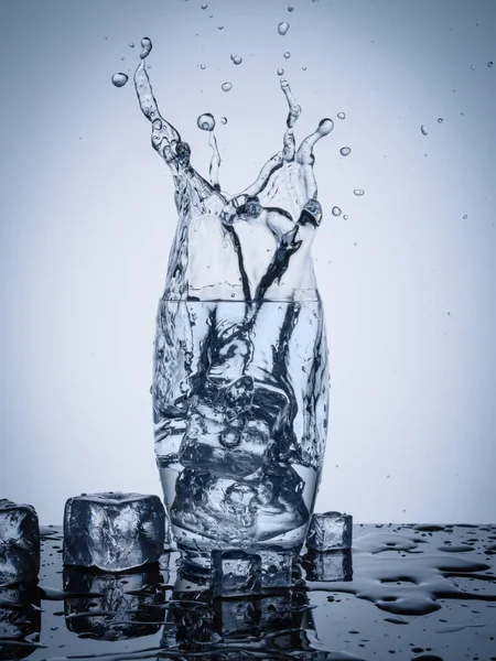 Rozprysk wody w szkle z kostkami lodu — Zdjęcie stockowe