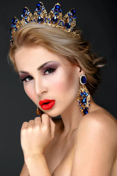 Mooie blonde meisje met een gouden kroon, oorbellen en professionele avond make-up — Stockfoto