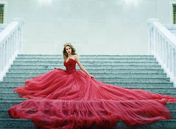 Young woman in a long red dress and gold crown sitting on the st — Stock Photo, Image