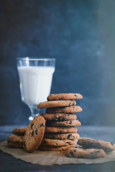 Печиво з шоколадом і склянкою молока на темному столі з сливою — стокове фото