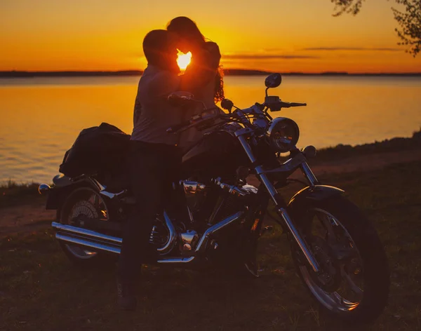 Two lovers with motorbike at sunset on the shore of the lake — Stock Photo, Image