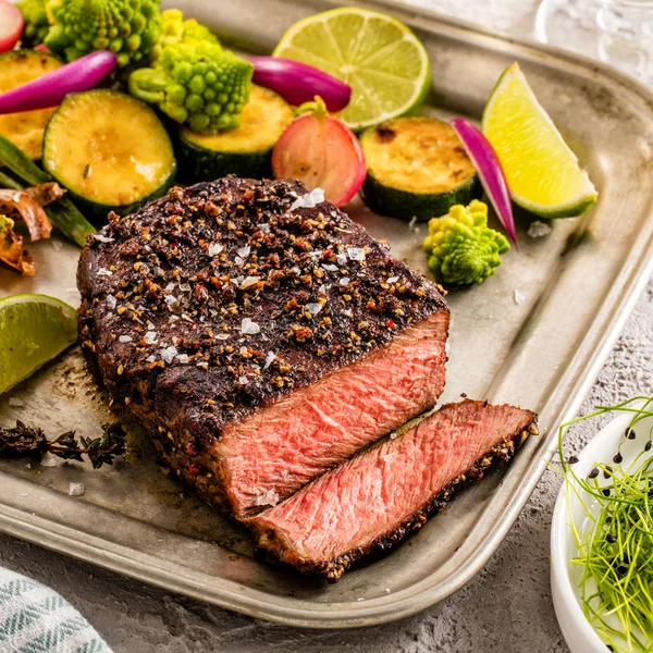 A grilled pepper steak garnished with lemon, onion and fresh her