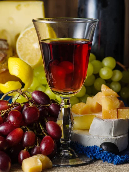 Um copo de vinho tinto com queijo e uvas na mesa — Fotografia de Stock