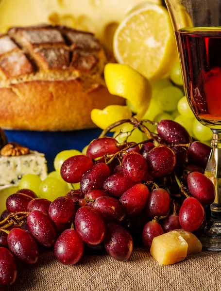 Uvas vermelhas com um copo de vinho e frutas na mesa . — Fotografia de Stock