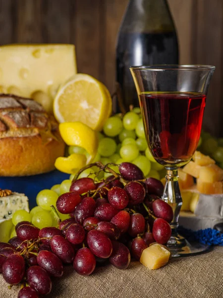 Um copo de vinho tinto com queijo e uvas na mesa — Fotografia de Stock