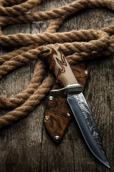 Hunting knife with a scabbard on a wooden surface with a rope. — Stock Photo, Image