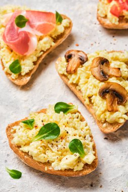 Omlet, pastırma, mantar, domates ve açık gri arka planda taze otlar.