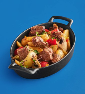 Kızarmış patates, et, mantar, soğan ve dolmalık biber mavi arka planda.