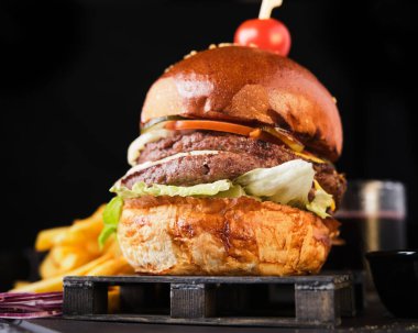 Koyu arkaplanda patates kızartması ve duble sığır etli çizburger.