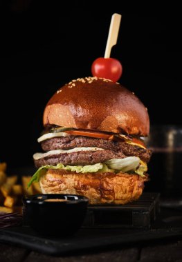 Koyu arkaplanda patates kızartması ve duble sığır etli çizburger.