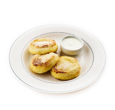 Ekşi kremalı peynirli kekler, beyaz tabakta pudra şekeri serpiştirilmiş. Süzme peynirli krep.