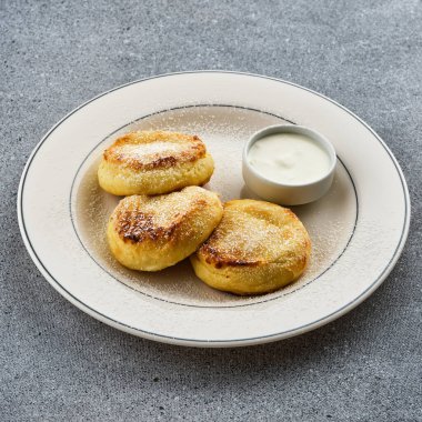 Ekşi kremalı peynirli kekler, beyaz tabakta pudra şekeri serpiştirilmiş. Süzme peynirli krep.