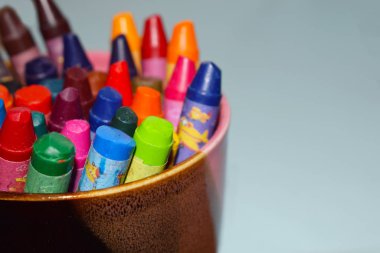 Mavi arka plandaki bir bardaktaki renkli kalemler.