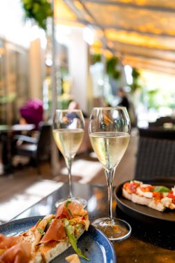 Yazlık terasta bruschetts 'li iki kadeh beyaz şarap, Bokeh güneş ışığı yapraklı kafe.