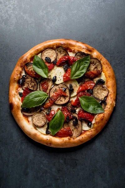 Italian pizza with eggplant basil cheese pepper and sauce on black background top view