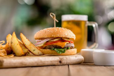 Biftek peynirli burger fesleğen soğan soslu patates ızgara soğan birası kağıt tahta tahta tahta tahta tahta tahta tahta tahta tahta ahşap kafe restoran terası bokeh