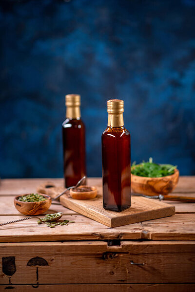 Две бутылки оливкового масла с миской оливок и салатом на деревянной доске вид сбоку
