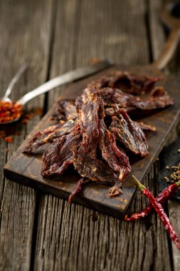 Ahşap tahtada kurutulmuş et ve baharatlı biber yapraklı mutfak manzarası.