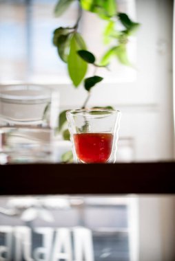 Bir bardak siyah filtre kahve güneş ışığının üzerine dökülüyor kahve evi yaprağı kafenin yan görüntüsünden ayrılıyor.