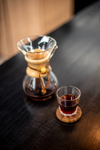 ケメックスフィルター付きブラックコーヒー醸造は ガラスハウスカフェの日光テーブルサイドビューに注ぎます — ストック写真