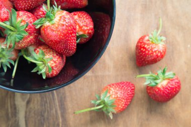 Ahşap masa üzerinde bir kase çilek.