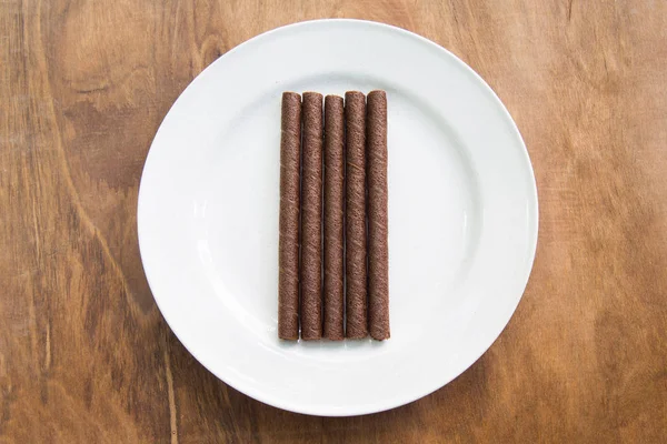 Rolos de wafer com chocolate em placa branca na mesa de madeira . — Fotografia de Stock