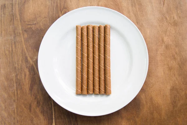 Rolos de wafer com chocolate em placa branca na mesa de madeira . — Fotografia de Stock