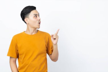Genç yakışıklı Asyalı adam, beyaz arka plandaki boşluğu işaret ederek şaşırıyor..