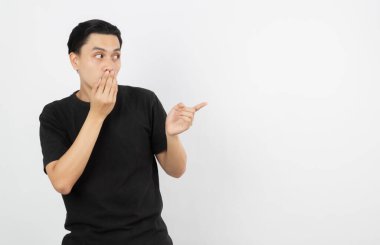 Siyah gömlekli genç Asyalı bir adam beyaz arka planda şaşırtıcı bir şekilde izole edilmiş bir şekilde beklerken bir ürünü ya da bir fikri sunmak için parmağıyla kenarı işaret ediyor..