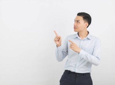 Mavi gömlekli genç Asyalı iş adamı beyaz arka planda sırıtırken bir yandan ürünü ya da fikri sunmak için parmağıyla kenarı işaret ediyor..