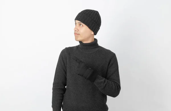 年轻英俊的亚裔男子 身穿灰色毛衣 头戴手套 头戴贝尼帽 手拿着手把旁边的东西放在白色背景上展示自己的产品或创意 — 图库照片