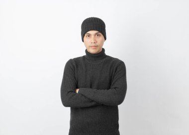 Beyaz arka planda mutlu bir yüzü olan kameraya bakarken gri kazak ve bere giyen genç Asyalı adam..