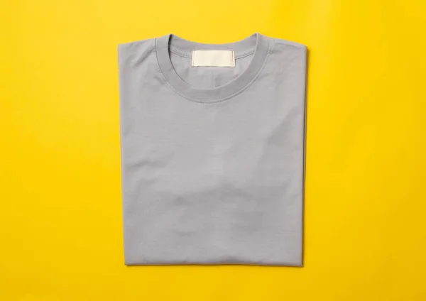 Grey folded t-shirt isolated on yellow background.