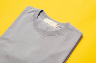 Tasarımınız için boş etiketli gri katlanmış tişört sarı arkaplanda izole edilmiş..
