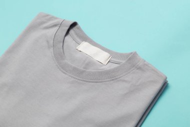Tasarımınız için boş etiketli gri katlanmış tişört mavi arkaplanda izole edilmiş..