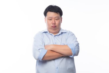 Mavi gömlekli Asyalı şişman adam kollarını kavuşturdu ve beyaz arka planda izole edilmiş kameraya bakıyor..