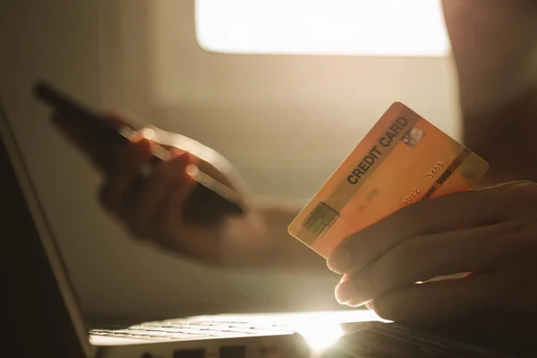 Male hands holding credit card and using smartphone at working desk for online shopping while break from work at home, E-commerce, Internet banking.