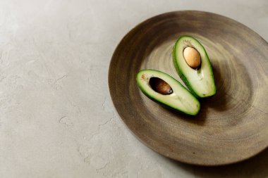 Gri arka planda kahverengi bir tabakta dilimlenmiş avokado.