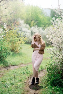 Çiçek açan kiraz bahçesinde yürüyen güzel genç bir kadın.