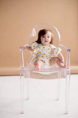 Şirin takım elbiseli kız bej arka planda, stüdyoda bir sandalyede oturuyor.