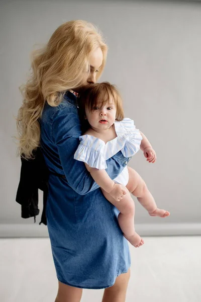 Stüdyo bej arka planda bebek sahibi genç bir anne sarışın.