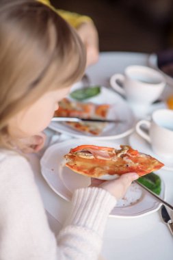 6 yaşındaki bir kız kafede pizza yiyor.
