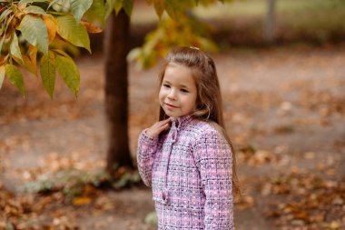 Komik kız. 5 yaşında. Sonbaharda parkta yürüyor.
