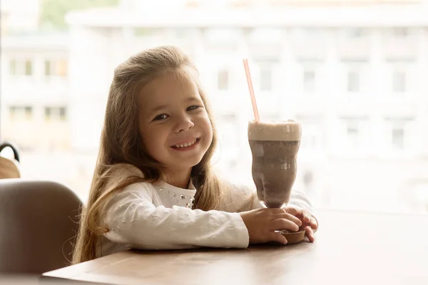 Funny girl 5 years old drinks hot chocolate with marfmellow in a cafe