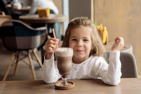 Komik kız. 5 yaşında. Kafede lokumlu sıcak çikolata içiyor.