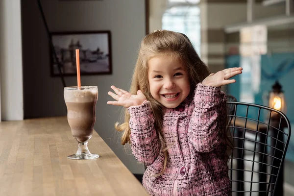 Funny girl 5 years old drinks hot chocolate with marfmellow in a cafe